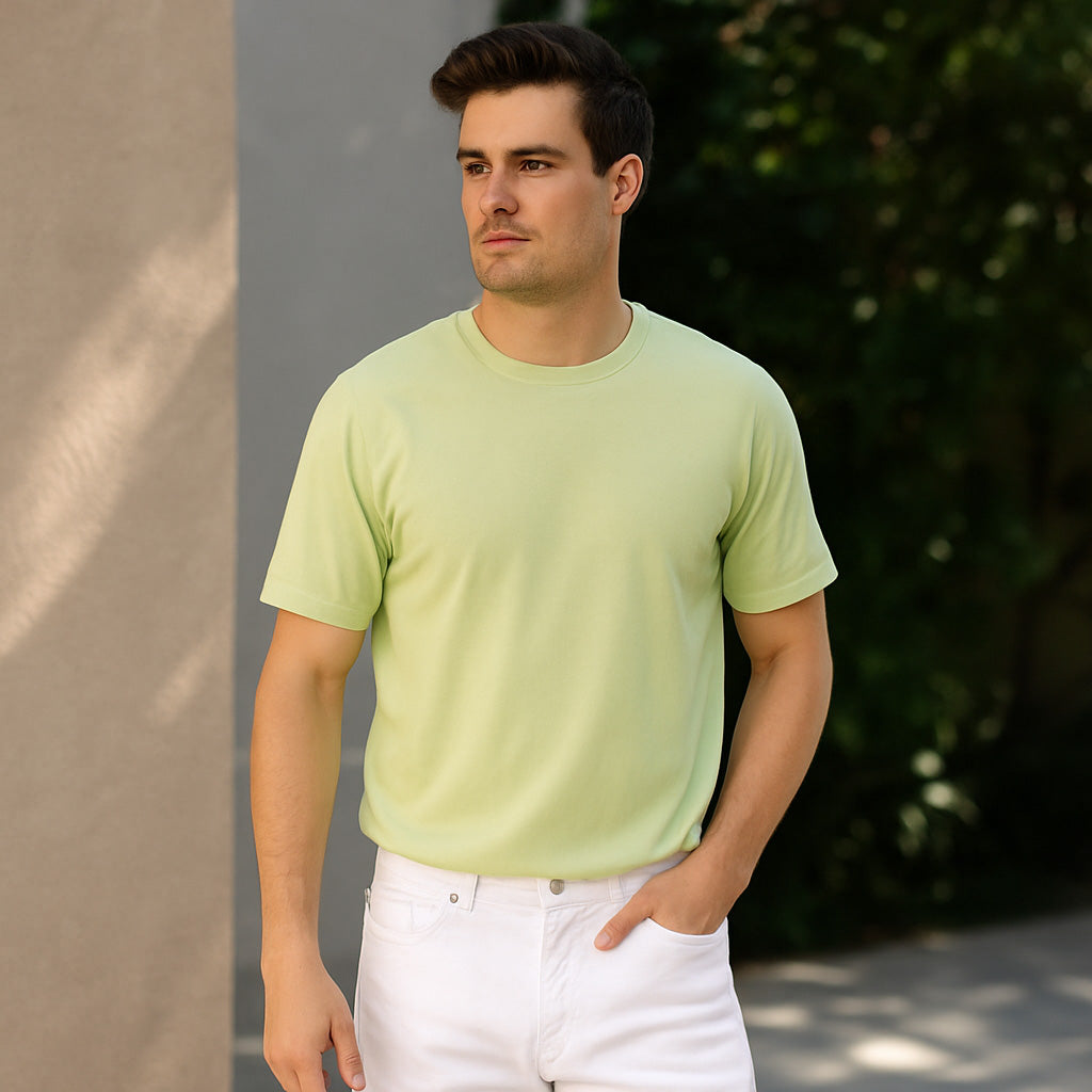 Young man wearing a pastel lime green t-shirt and beige trousers, standing casually on a sunlit sidewalk with a relaxed vibe, captured in a real-life streetwear setting
